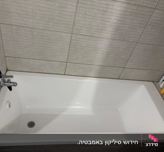 אמבטיה לבנה בחדר רחצה עם איטום סיליקון בחיבורי הקיר